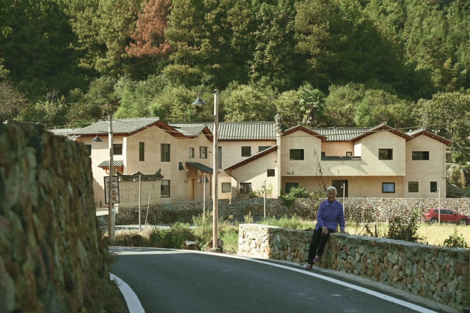从公共接待区路边看17、18、19号楼,阿婆坐在石挡墙边 / Buildings 17, 18 and 19 seen from the road by the public reception area, with an elderly resident seated beside the stone retaining wall